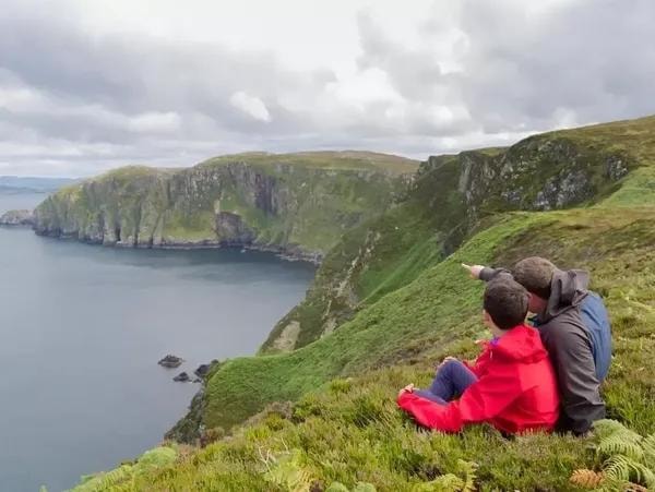 Two people sitting on coastal cliffs overlooking the sea